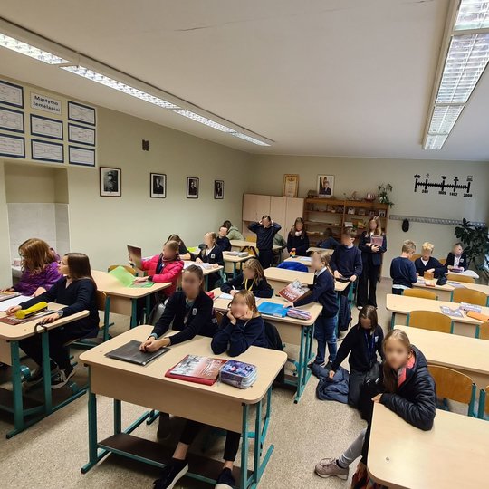 Nuotraukoje matomi mokiniai, kurie yra istorijos kabinete. Dalis mokinių sėdi, o kita dalis stovi, dedasi daiktus į kuprines.