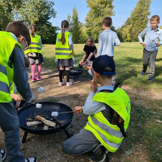 Grupė vaikų ryškiomis atšvaitinėmis liemenėmis pozuoja nuotraukai prie Gedimino paminklo Katedros aikštėje. Šalia jų stovi jų auklėtoja, fone matosi giedras dangus, varpinė ir katedra.