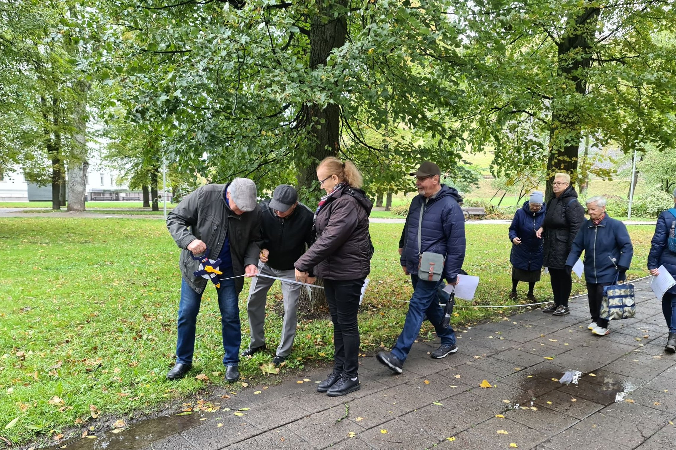 Nuotrauka daryta Pilių parke, prie Valdovų rūmų. Ekskursijos grupė tyrinėja Vilniaus pilių žemėlapius, naudojantis kompasu ir metru bando atrasti nurodytas vietas. Nepaisant blogo oro, nes ant pėsčiųjų kelio matosi balos, jie linksmai ieško užduočių atsa