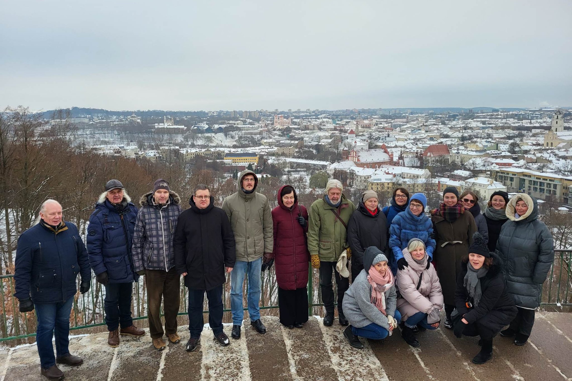 „Lietuvos nacionalinis kultūros centras“ kolektyvas pozuoja nuotraukai priešais Trijų Kryžių paminklą. Už nugaros matosi Vilniaus panorama su apsnigusiais stogais.
