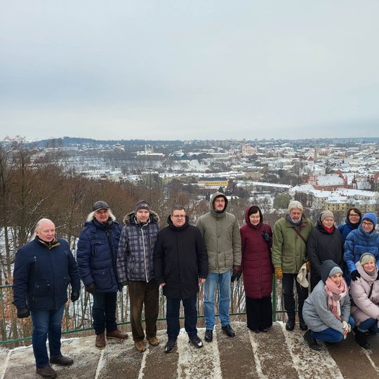„Lietuvos nacionalinis kultūros centras“ kolektyvas pozuoja nuotraukai priešais Trijų Kryžių paminklą. Už nugaros matosi Vilniaus panorama su apsnigusiais stogais.