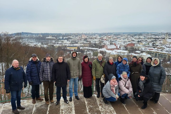 „Lietuvos nacionalinis kultūros centras“ kolektyvas pozuoja nuotraukai priešais Trijų Kryžių paminklą. Už nugaros matosi Vilniaus panorama su apsnigusiais stogais.