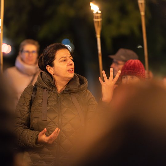 Gidė tarp ekskursijos dalyvių, kurie laiko fakelus.