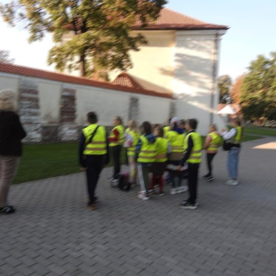 Matome vaikų grupelę, esančią su juos vedančia gide. Jie stovi priešais Lietuvos nacionalinį muziejų.