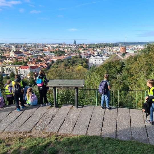 Filaretų mokyklos ketvirtokai keliautojai pagaliau pasiekę paskutinį kelionės tašką, ant aukšto kalno, iš viršaus žiūri į Vilniaus miesto kraštovaizdį. Vaikai įdėmiai apžiūrinėja kiekvieną Vilniaus senamiesčio pastatą bei besipuikuojančią ant kito kalno G