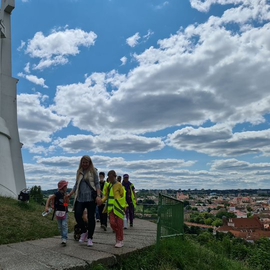 Stovyklautojai ir jų vadovė prie Trijų kryžių kalno paminklo, susikibę už rankų.