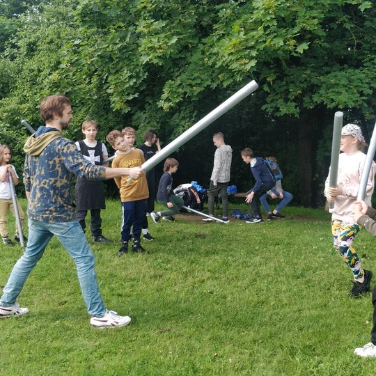 Moksleiviai ir auklėtojas tarpusavyje kaunasi su putplasčio lazdomis.