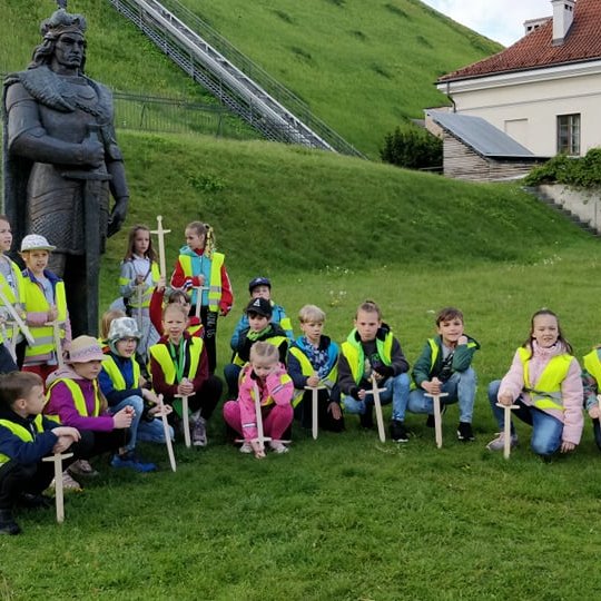 Vaikai su mediniais kalavijais pozuoja šalia Vytauto statulos.