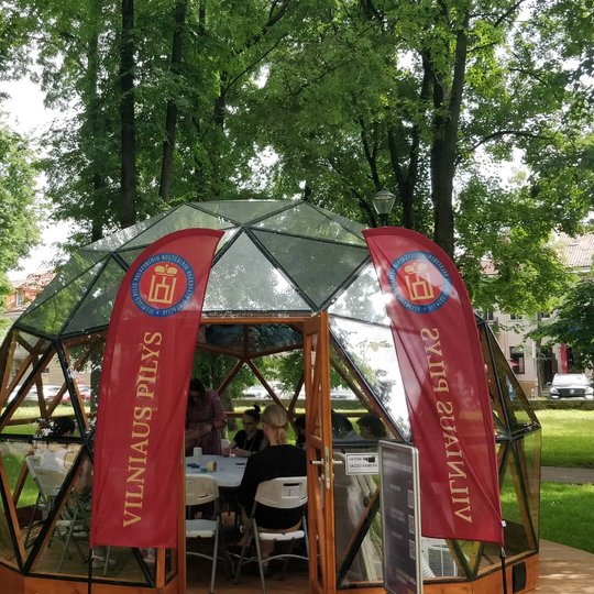 Iš lauko nufotografuotas Vilniaus pilių kupolas, pilnas mazgus rišančių žmonių.