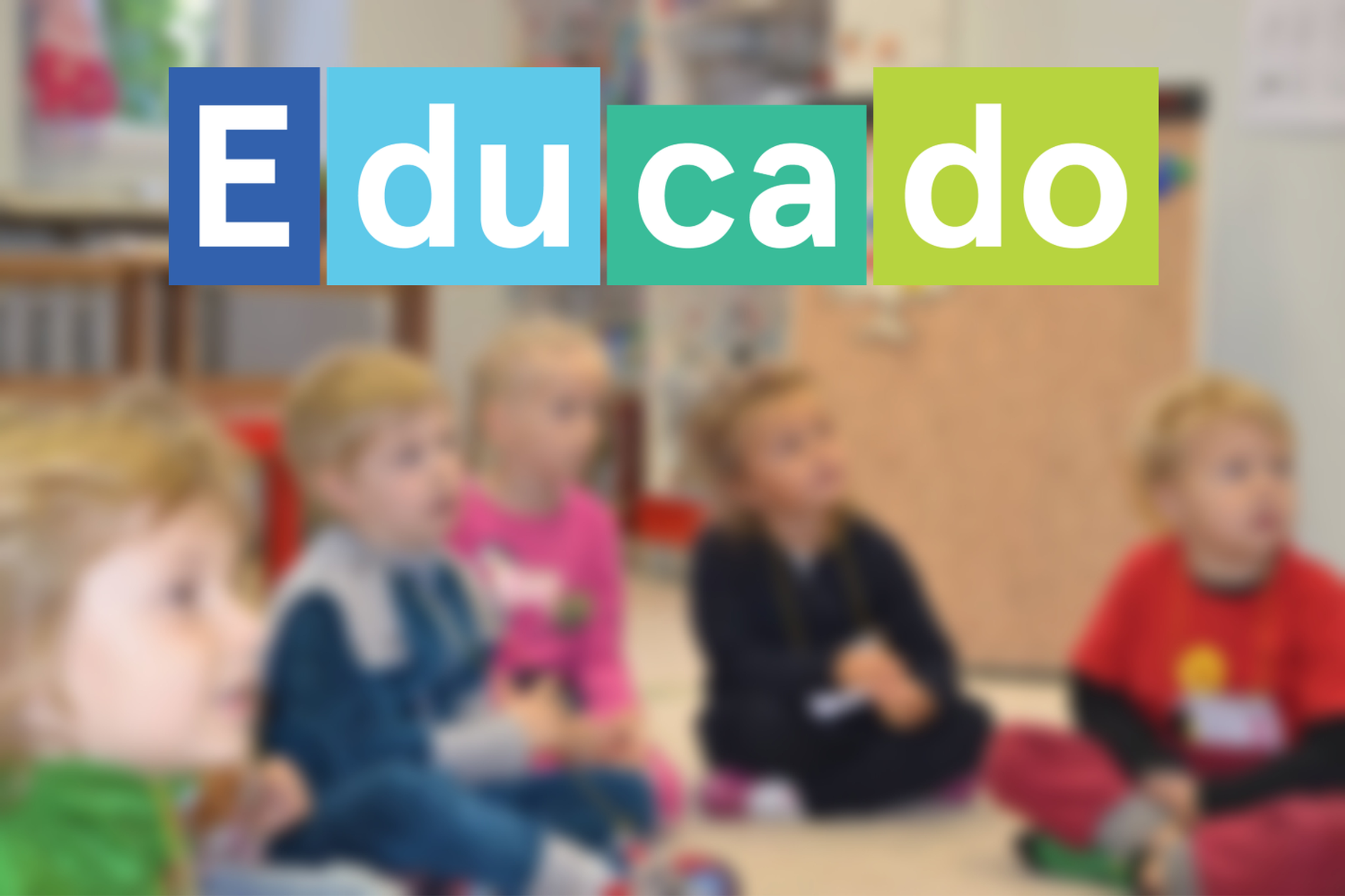 Darželinukai, susėdę ant kilimuko, įdėmiai klausosi. Nuotraukos apačioje "Educado" logotipas, kuris susidėta iš skirtingų spalvų ir didžio kaladėlių.