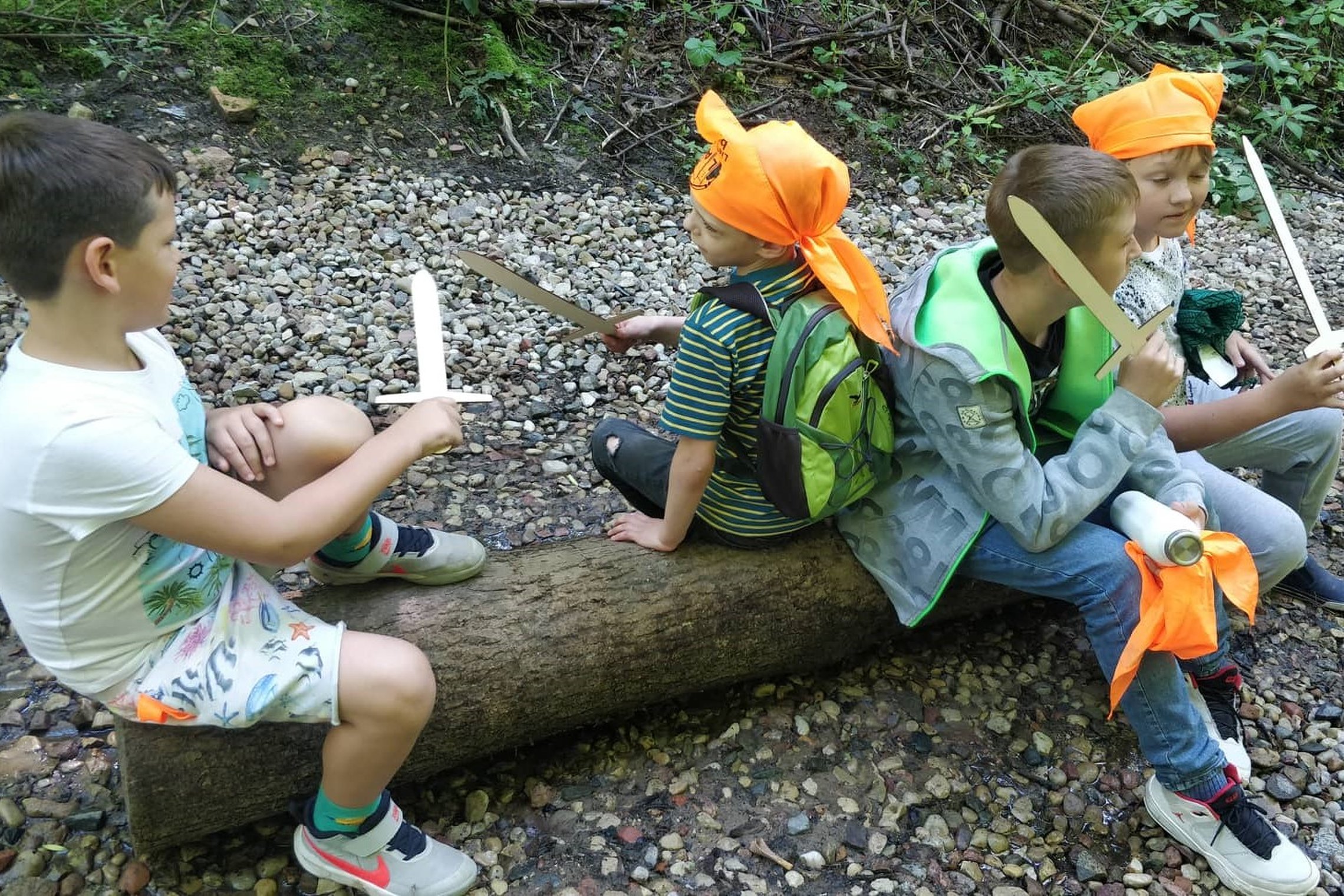 Vaikai, su mediniais kalavijais, prisėdę pailsėti ant raisto Kreivosios pilies teritorijoje.