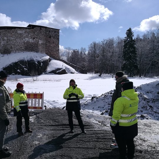 Rezervato darbuotojai kartu su kolegomis iš Suomijos. tolumoje matosi mūrinė pilis.