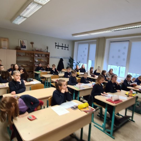 Istorijos pamoka. Mokiniai sėdi klasės suoluose, klausosi mokytojos pasakojimo.