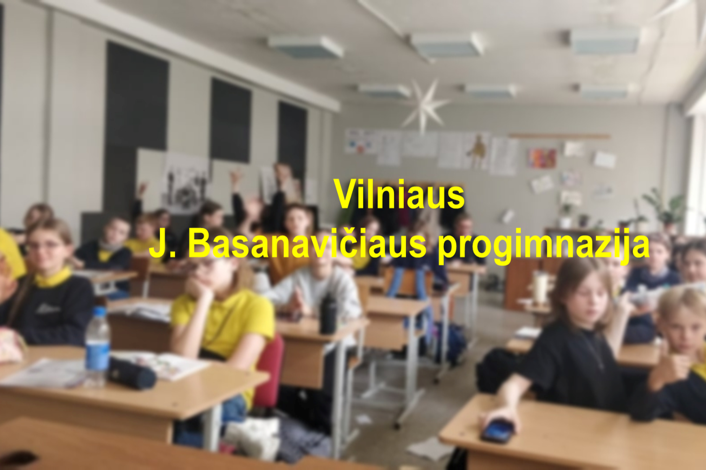 Moksleiviai klasėje, priekyje nuotraukos geltonoms raidėmis parašyta "Vilniaus J. Basanavičiaus progimnazija".