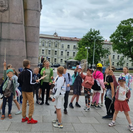 Vaikai, karingai nusiteikę, kelia medinius kardus į viršų.