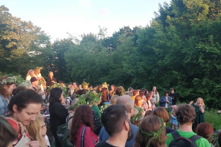 Gausi žmonių minia, kai kurie su žolių vainikais, klausosi smuikininko ir vokalistės koncerto. 