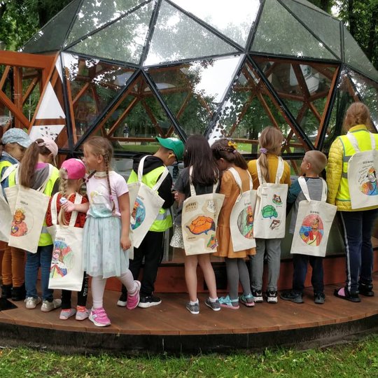 Vaikai, su medžiaginiais maišeliais ant nugaros, pozuoja nuotraukai šalia Vilniaus pilių kupolo.