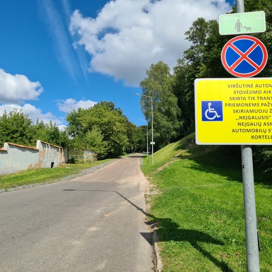 Asfaltuotas kelias link Kreivosios pilies teritorijos, šalia kelio ženklas apie stovėjimo aikštelės specifikas.