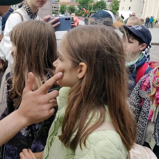 Kareivis maskuojamaisiais dažais dažo mergaitei žandą.