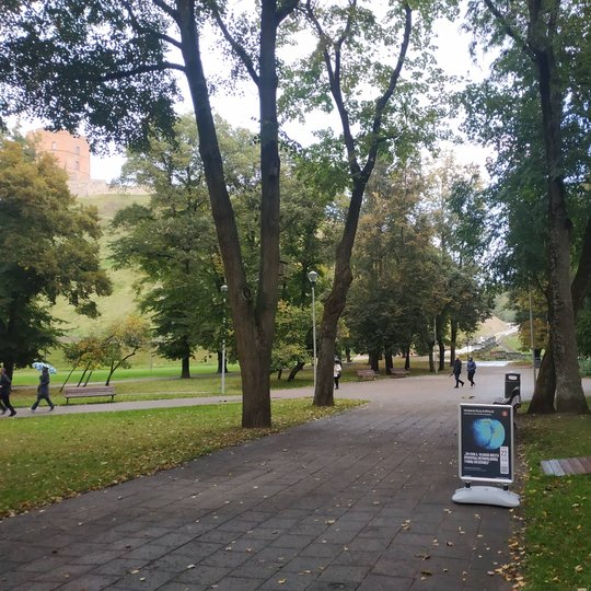 Vilniaus pilių kupolas iš lauko. Šalia stovi stendas su paskaitos afiša. Matosi Gedimino kalnas ir pilis.
