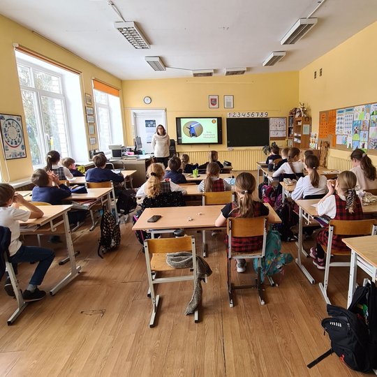 Trečiokų klasė, fotografuota iš klasės galo. Priekyje stovi edukatorė.
