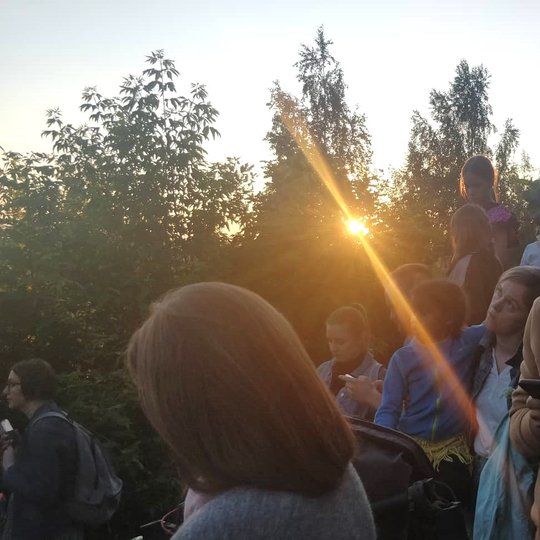 Žmonės prietemoje, medžių paunksmėje.