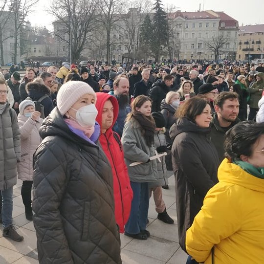 Susirinkusių žmonių minia Katedros aikštėje. Žmonės apsirengę žiemiškai. Kai kurie žmonės rankose laiko medinius kalavijus.