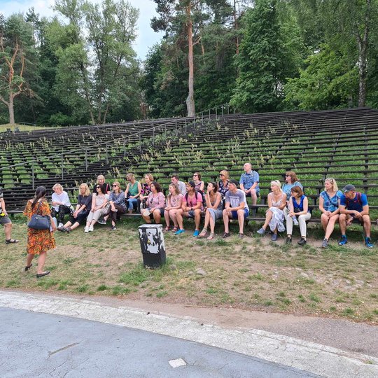 Ekskursijai tęsiantis, dalyviai klausėsi Kalnų parko istorijos susėdę ant estrados suolų.