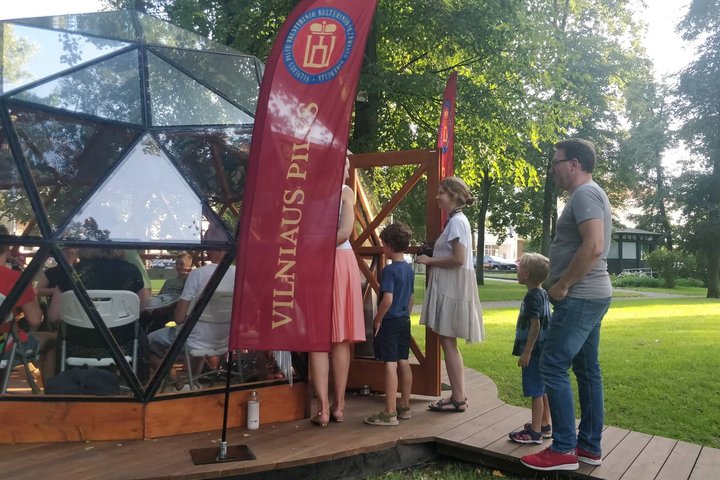 Žmonių kupinas Vilniaus pilių kupolas. Šalia kupolo žmonės smalsiai domisi kas jame vyksta.