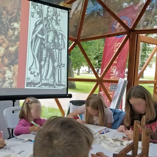 Vilniaus pilių kupole vaikai spalvina maišelius su Lietuvos valdovų atvaizdais. Kairėje skaidrė su vokiečių ordino magistru - Ulrichu fon Jungingenu.