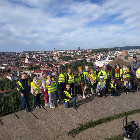 Antrokai mokiniai pozuoja nuotraukai priešais Trijų Kryžių paminklą. Jiems už nugarų Vilniaus senamiesčio panorama.