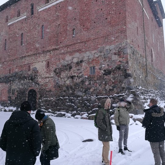 Rezervato darbuotojai kartu su kolegomis iš Suomijos šalia pilies. Aplink apsnigta.