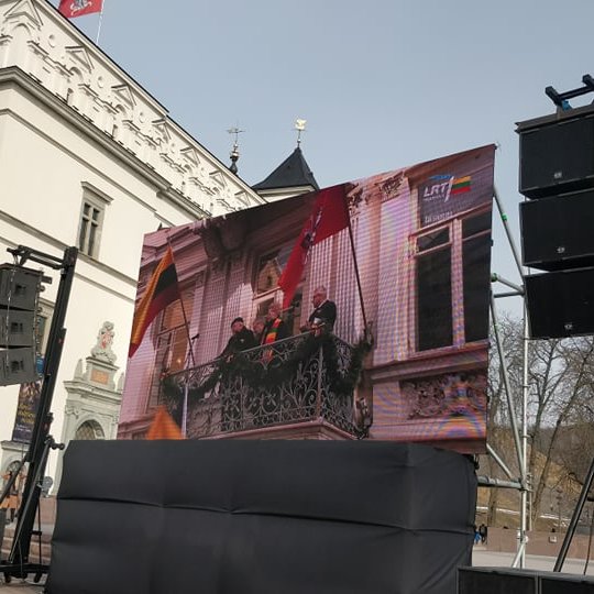 Ekranas su kolonėlėmis Katedros aikštėje, tarp Valdovų rūmų ir Gedimino paminklo. Ekranas transliuoja šventinė kalbą.