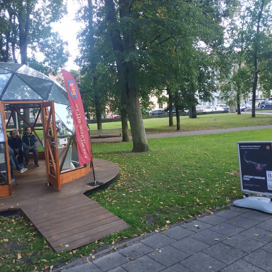 Vilniaus pilių kupolas iš lauko. Kupole vyksta paskaita, šalia kupolo stendas su paskaitos afiša.