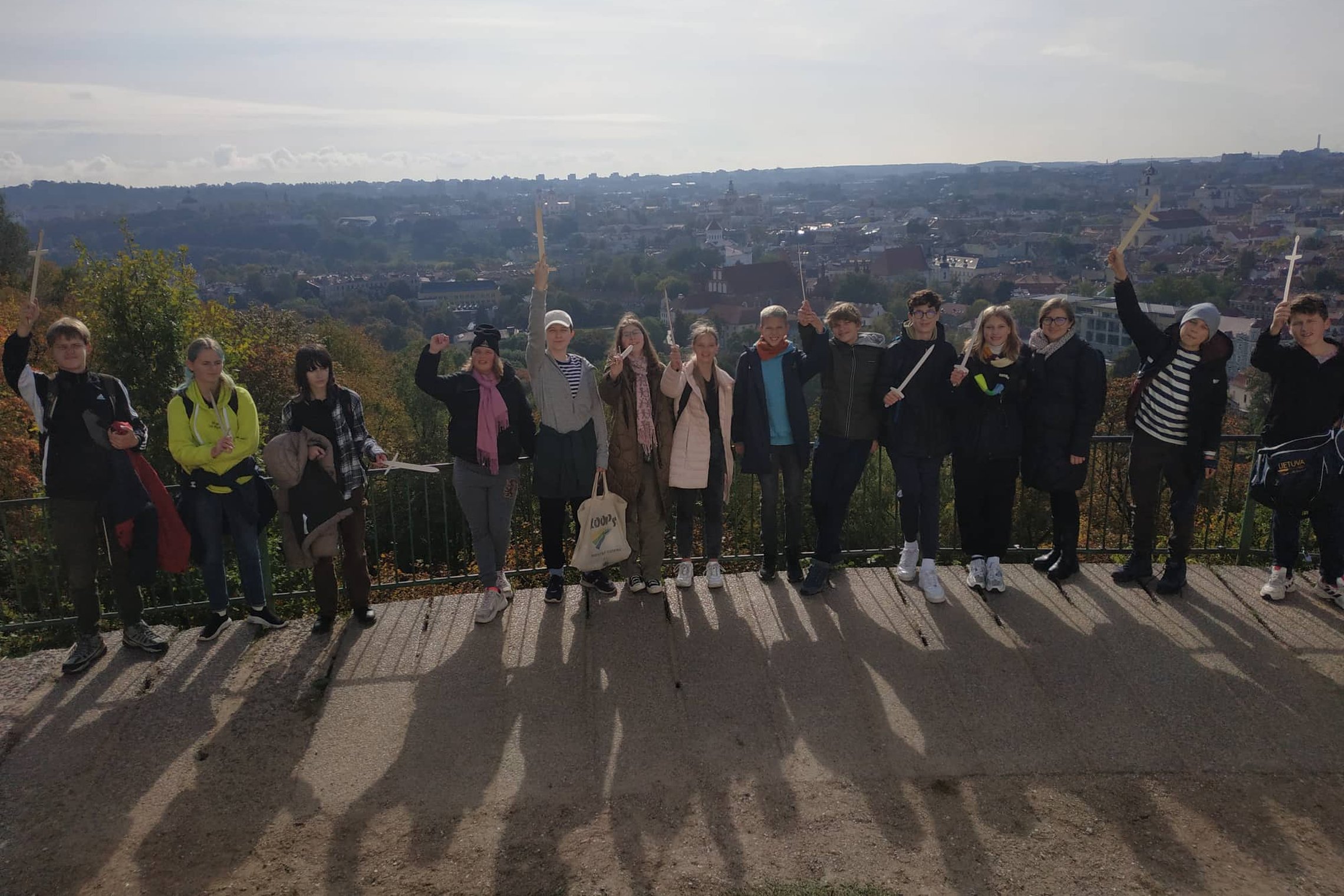 Šaltinėlio mokyklos septintokai pozuoja nuotraukai su mediniais kalavijais ant Trijų Kryžių kalno. Jiems už nugarų Vilniaus panorama.