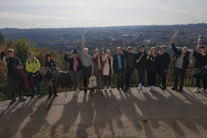 Šaltinėlio mokyklos septintokai pozuoja nuotraukai su mediniais kalavijais ant Trijų Kryžių kalno. Jiems už nugarų Vilniaus panorama.
