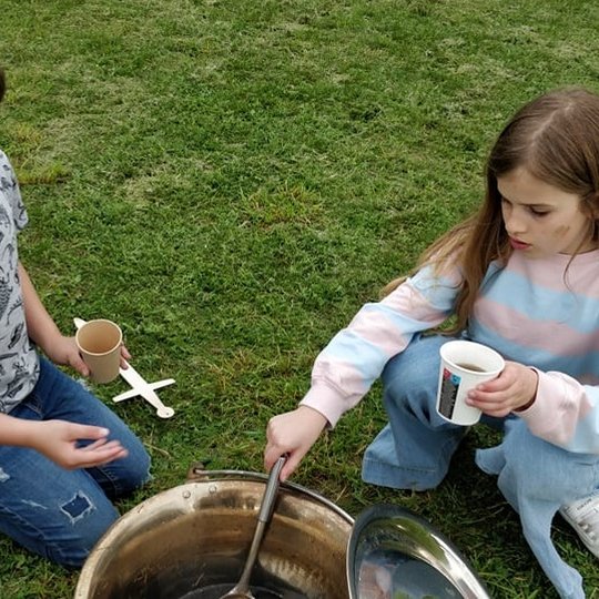 Mergaitė su berniuku pilasi arbatos iš geležinio katilo.