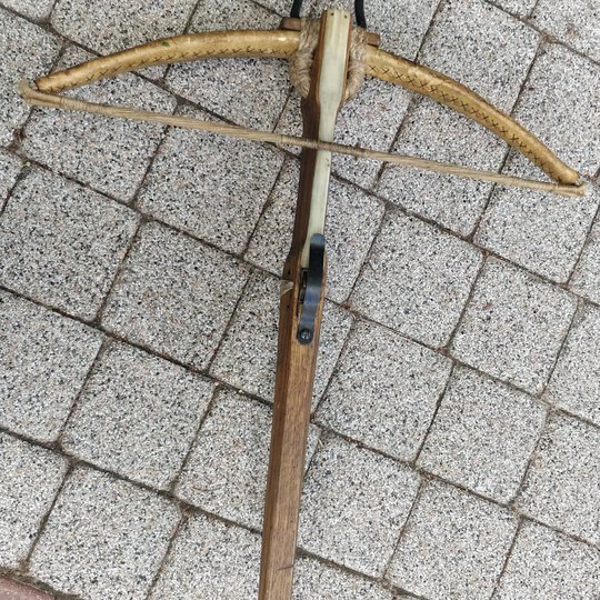 Medinis viduramžinis arbaletas padėtas ant akmeninių grindinio plytelių.