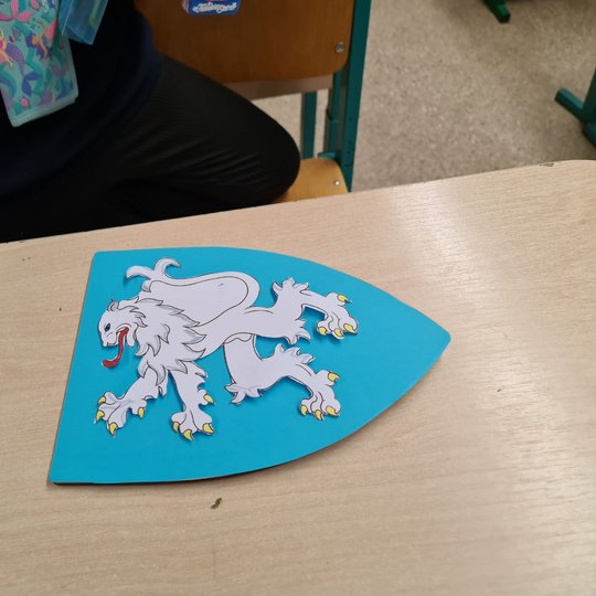 Mėlynas herbas su baltu liūtu ant klasės suolo.
