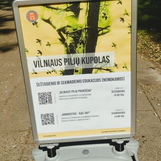 Renginio afišos stendas šalia Vilniaus pilių kupolo.
