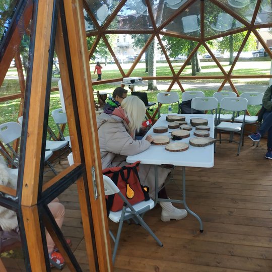 Vilniaus pilių kupole susirinkę lankytojai sėdi prie stalo ir apžiūrinėja medžio rievės.