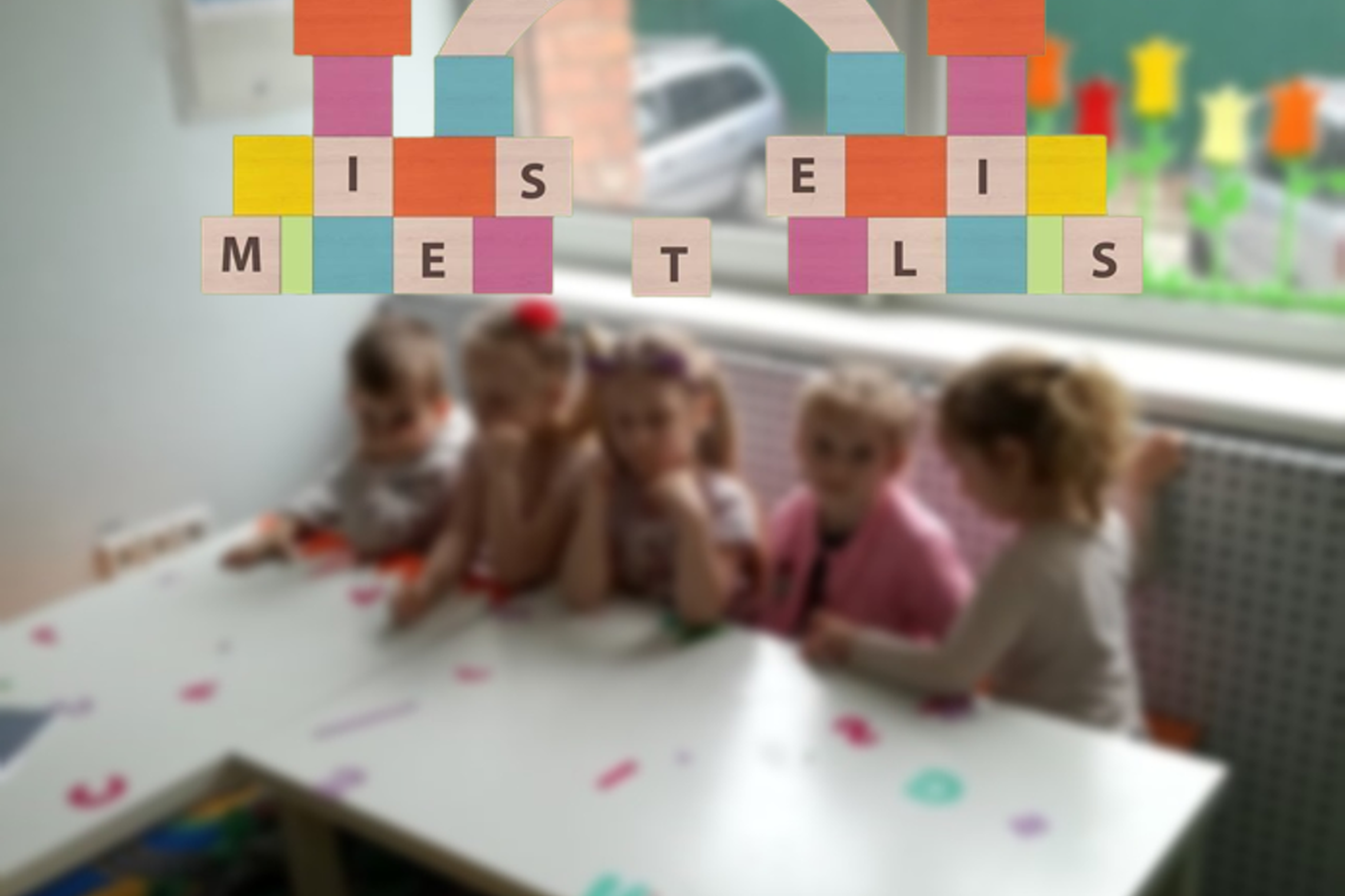 Darželinukai sėdi prie stalo klasėje. Nuotraukos priekyje darželio „Kaladėlių miestelis" logotipas.