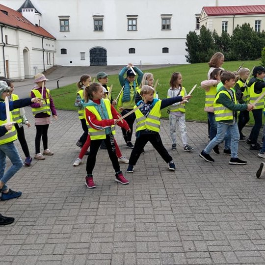Vaikai su atšvaitinėmis liemenėmis ir mediniais kalavijais Nacionalinio muziejaus vidiniame kieme. 