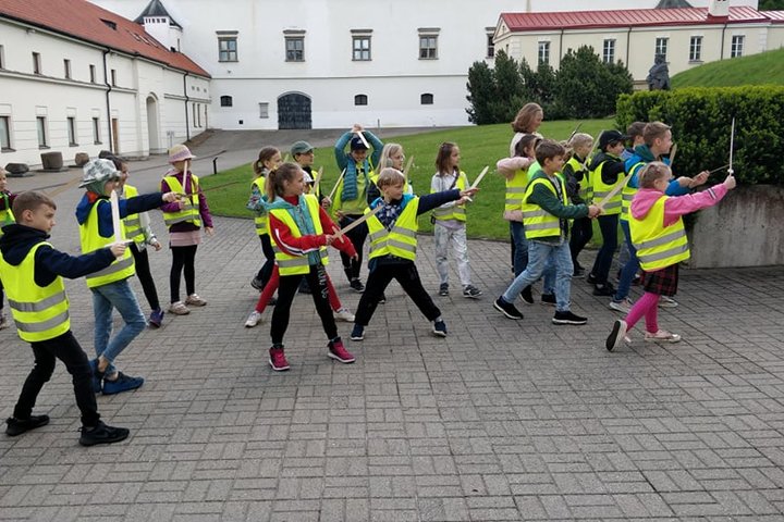 Vaikai su atšvaitinėmis liemenėmis ir mediniais kalavijais Nacionalinio muziejaus vidiniame kieme.