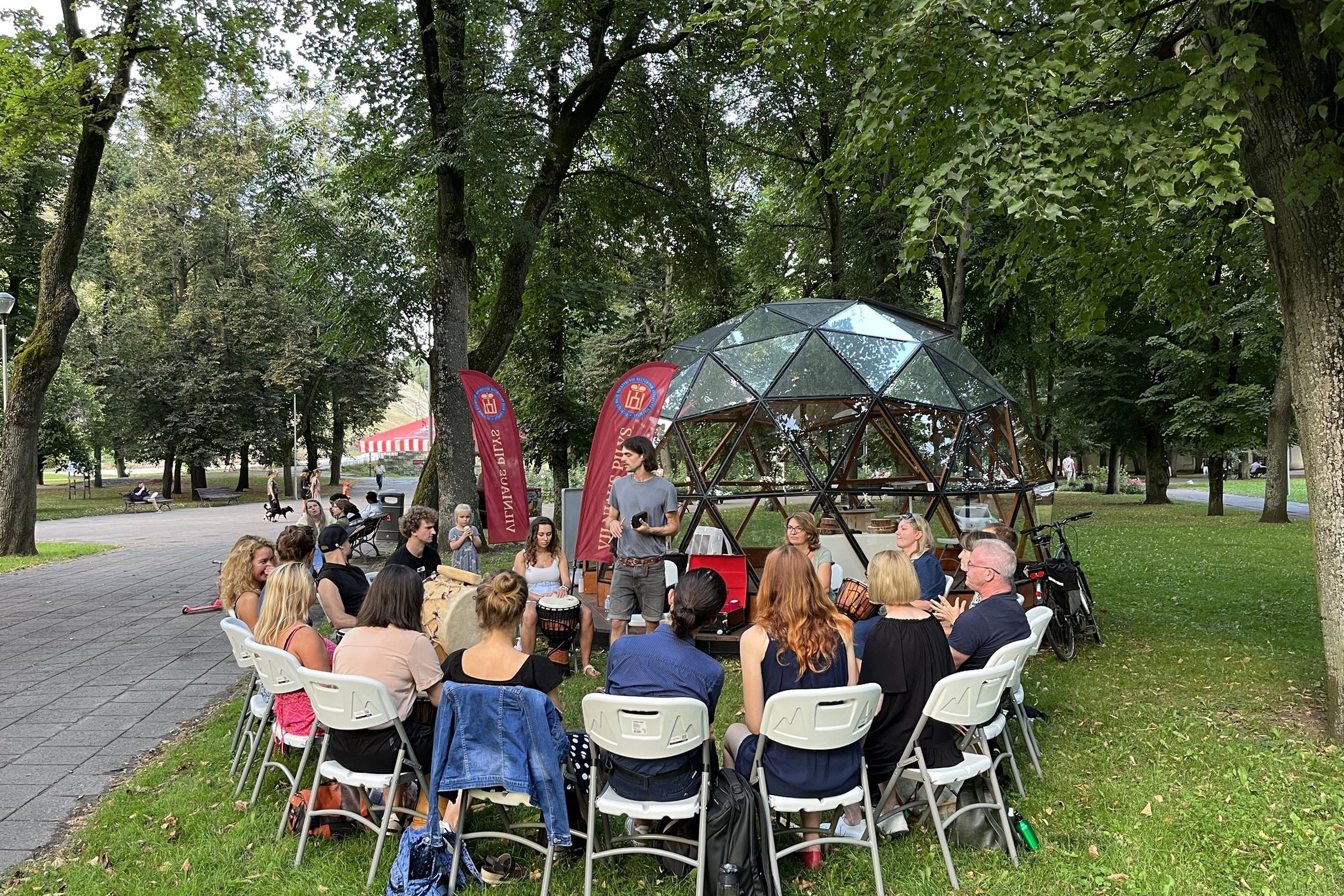 Šalia Vilniaus pilių kupolo užsiėmimo dalyviai, susėdę ratu ant baltų kėdžių ritmingai mušą būgnus.