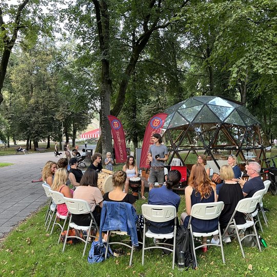 Šalia Vilniaus pilių kupolo užsiėmimo dalyviai, susėdę ratu ant baltų kėdžių ritmingai mušą būgnus.