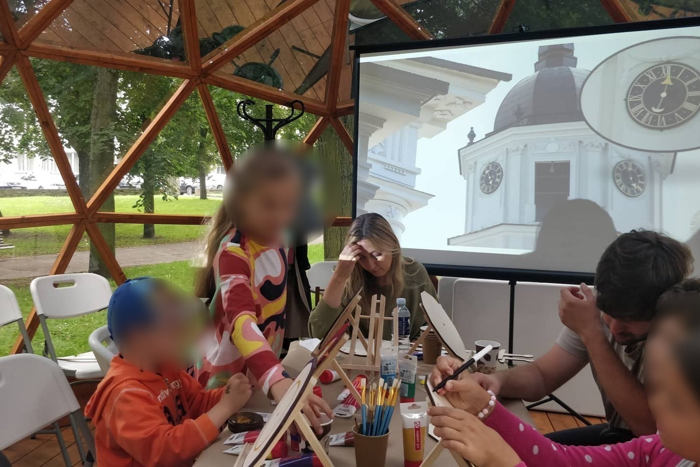 Vilniaus pilių kupole vaikai su tėvais spalvina laikrodžius. Projektoriuje skaidrė su Katedros varpinės laikrodžiu.