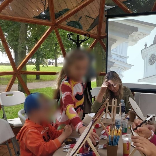 Vilniaus pilių kupole vaikai su tėvais spalvina laikrodžius. Projektoriuje skaidrė su Katedros varpinės laikrodžiu.