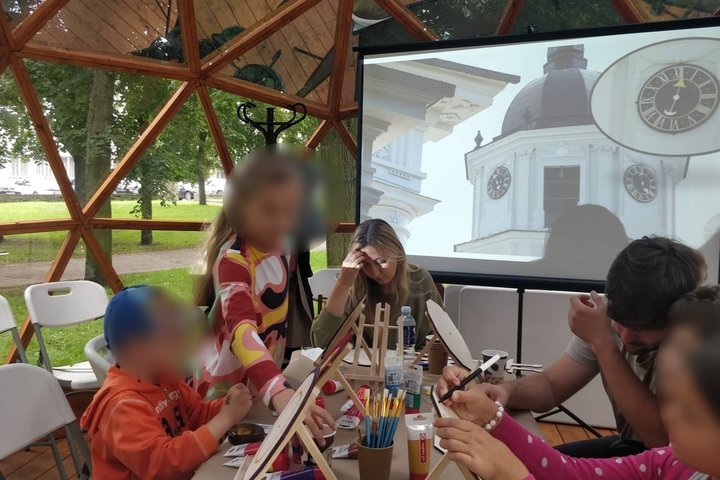 Vilniaus pilių kupole vaikai su tėvais spalvina laikrodžius. Projektoriuje skaidrė su Katedros varpinės laikrodžiu. 