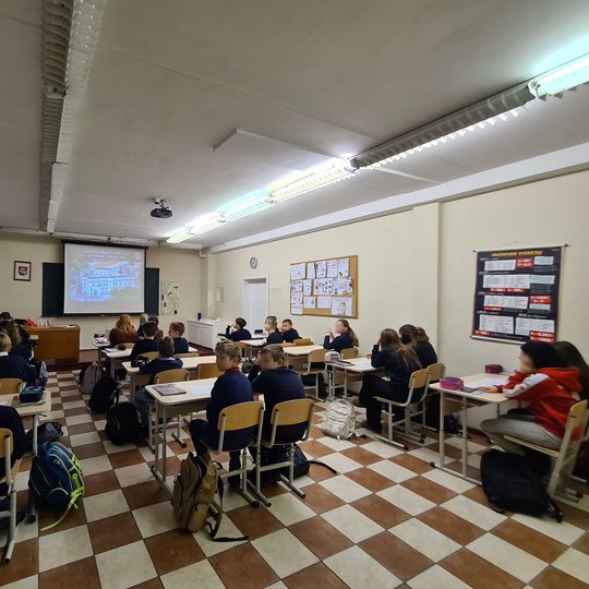Klasėje mokiniai klausosi istorijos pamokos. Pora jų atsisukę į kamerą.